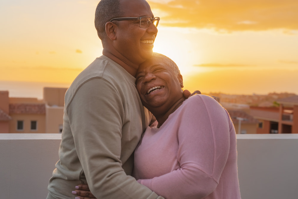 Older black couple hugging happily during sunset