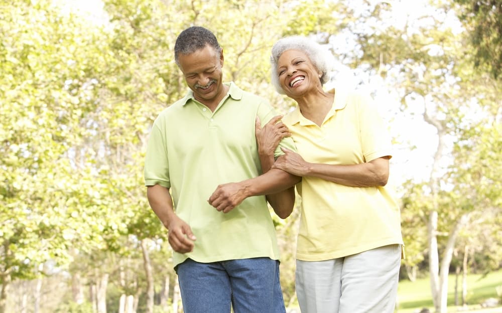 Older black couple laughing and smiling while walking in the park